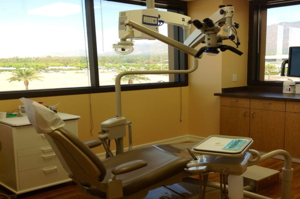 Modern dental examination room with chair, overhead light, and panoramic window overlooking landscape.