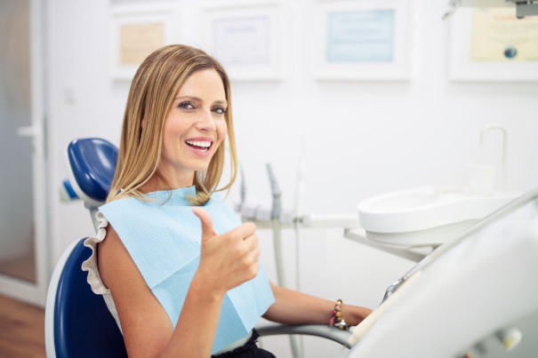 Woman in dental chair holding blue bib, smiling at dentist's office.